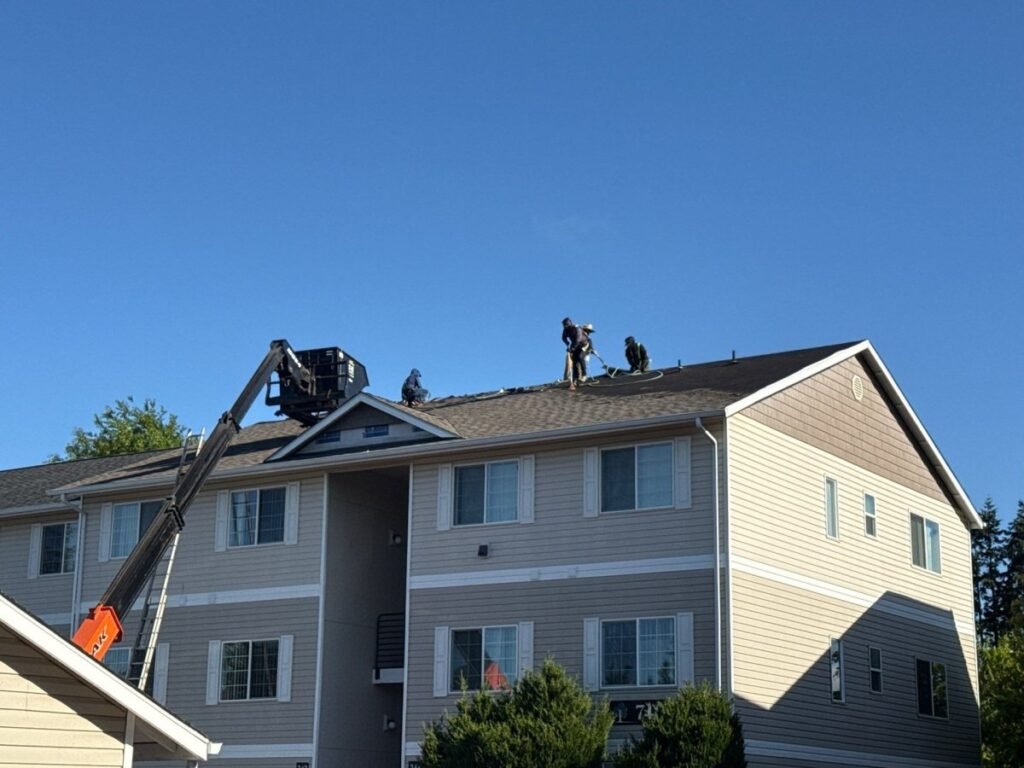 Professional roofing contractors using boom lift to work on multi-story apartment roof